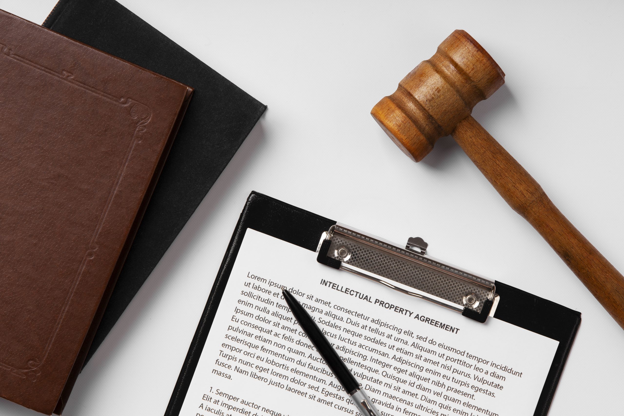 Drewniany młotek sędziowski, clipboard z dokumentem i długopisem oraz dwie książki na białym tle. Postępowanie gospodarcze.